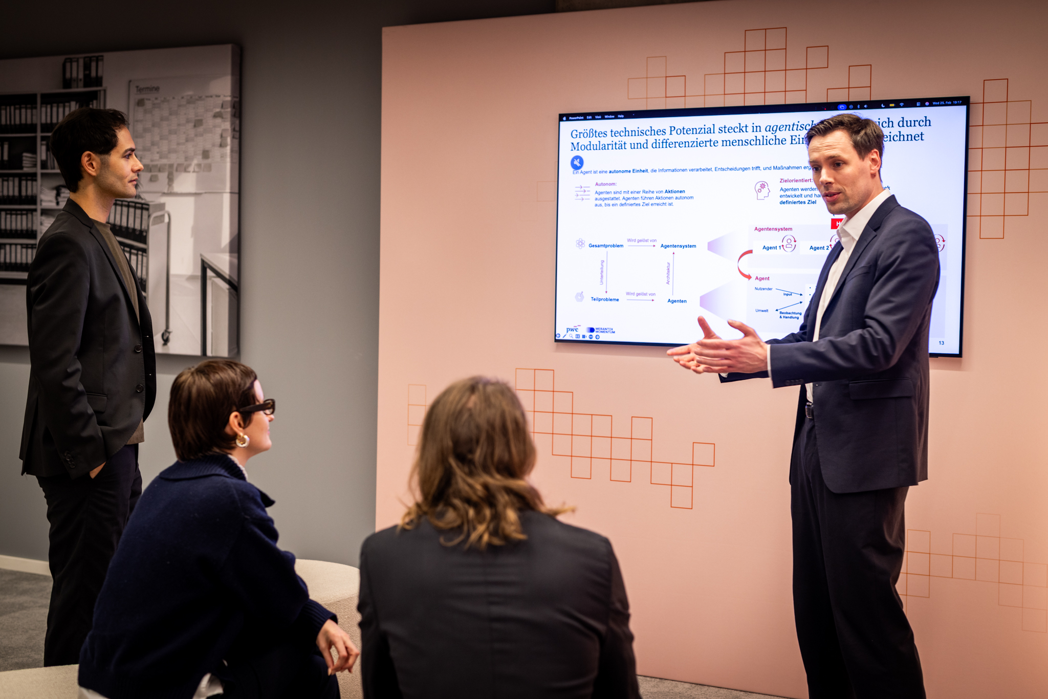 Ein Teilnehmender praesentiert am Bildschirm KI-Anwendungsbeispiele, waehrend drei weitere Teilnehmende aufmerksam folgen